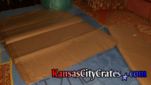 Blankets are laid out on floor before placing brown paper used to wrap items for crating.