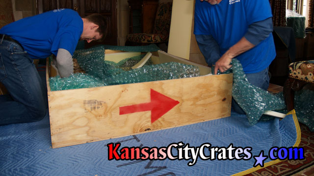 Wood export crate laying on furniture blanket with craters packing bubble wrap and foam inside to protect it.