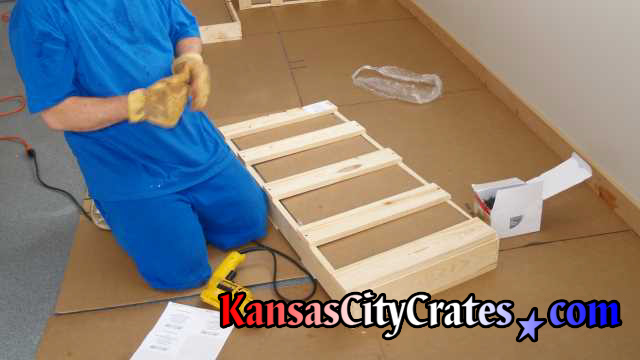 Crater closing domestic slat crate while working on cardboard in garage.