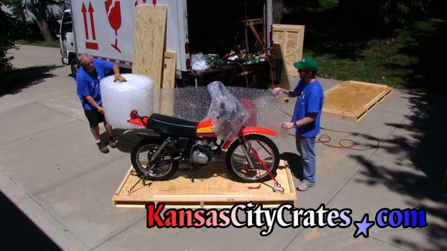Personnel wrap dirt bike in bubble wrap to protect it during crating
