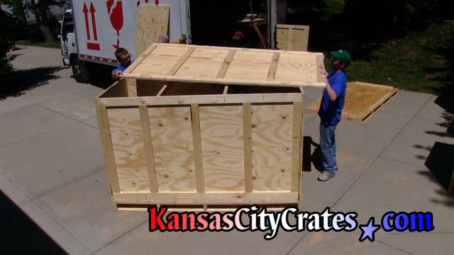 2 staff members move large lid of crate into position for closing of crate