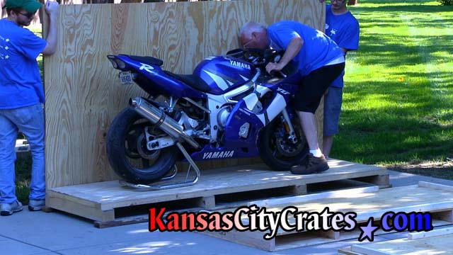 Personnel placing sidewall of crate onto pallet to check position of  motorcycle
