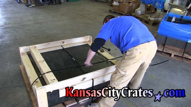 Granite base protected by open frame style crate being steel banded to rough oak shipping pallet.