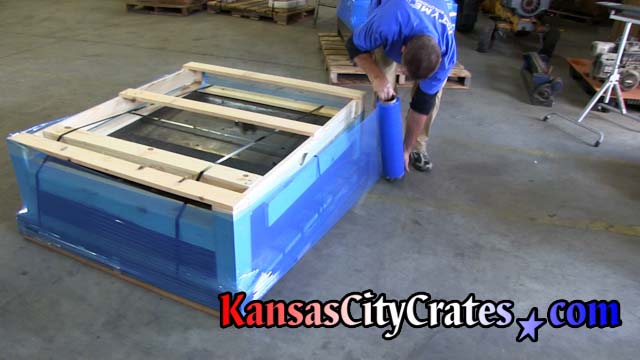 Stretch wrapping open frame crate steel strapped onto pallet with corner guards.